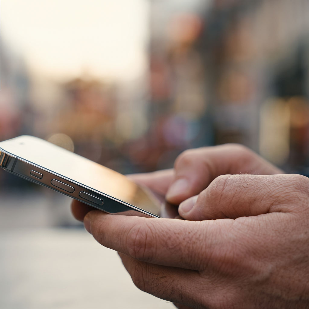 Close-up of a hand checking a smartphone with a bright screen glare, representing a customer reached by our digital marketing services.